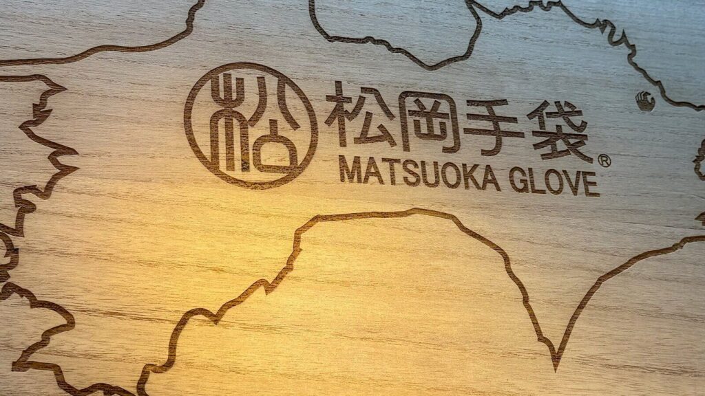 Engraved wooden display at the Matsuoka Glove booth, featuring an outline of Shikoku as a nod to their home in Kagawa Prefecture